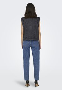 Μαύρο τζιν γιλέκο χωρίς μανίκια με εφαρμοστή γραμμή, που διαθέτει μεγάλα ανοίγματα για τα χέρια και μυτερή ραφή στην πλάτη. Συνδυασμένο με μπλε τζιν ψηλόμεσα.