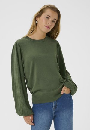 Maglione verde con scollo rotondo e maniche a palloncino texturizzate, abbinato a jeans blu. Il tessuto sembra morbido e leggero.