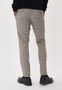Svetlo sivi karirani hlače z diskretnimi oran�žnimi črtami, slim fit, z dvema zadnjima žepoma, v kombinaciji s črnimi natikači in teksturirano črno puloverjem.