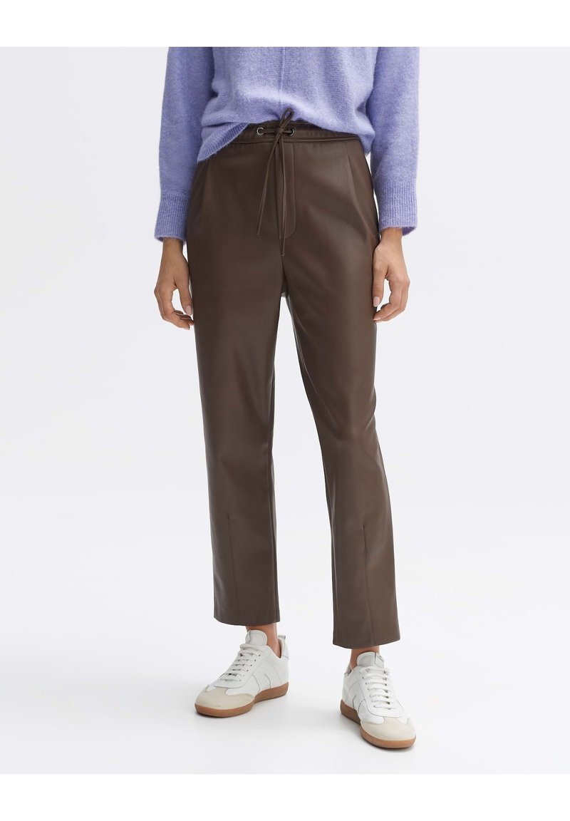 Personne portant un pantalon droit marron foncé avec une taille à cordon, un pull violet clair et des baskets blanches avec des semelles en gomme.