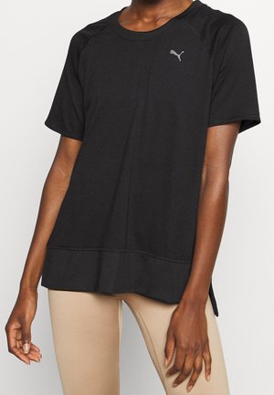 Personne portant un t-shirt noir Puma ample à manches courtes et des leggings beige, debout devant un fond clair.