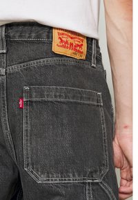 Vue de dos d'une personne portant un jean Levi's noir montrant la poche arrière, l'étiquette rouge Levi's et le patch en cuir avec les détails de la taille.