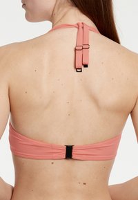 Kvinde set bagfra iført en lyserød halterbikini-top med justerbare stropper bundet ved halsen og en sort spænde bagpå.