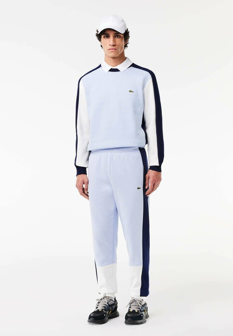 Sweatshirt bleu clair avec des rayures bleu marine et blanches, joggers bleu clair assortis, et une casquette blanche. Présente un petit logo vert sur la poitrine.