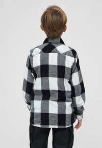 Fekete-fehér kockás flaneling, gombos gallérral, hosszú ujjakkal és laza fazonnal, kontrasztos kockás mintázattal.