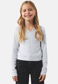 Grå langærmet top med ribbet tekstur og V-hals, suppleret med tre små knapper. Sammen med mørke denim jeans med blomstermønster.