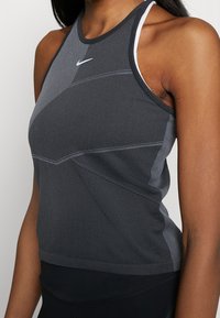 Sportovní tank top Nike v tmavě šedé barvě, s texturovanou tkaninou, designem se závodním zádovým střihem a reflexními detaily. Doplněný malým logem.