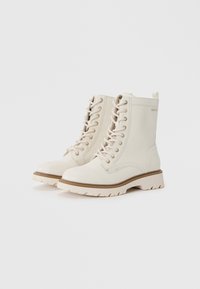 Botas blancas de cordones con una superficie texturizada, que cuentan con una suela de goma resistente y una entresuela en tono marrón claro que contrasta. El diseño incluye una pequeña lengüeta.