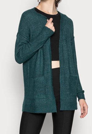 Cardigan turchese realizzato in materiale morbido, caratterizzato da una vestibilità comoda, apertura frontale, polsini a coste e due tasche frontali.
