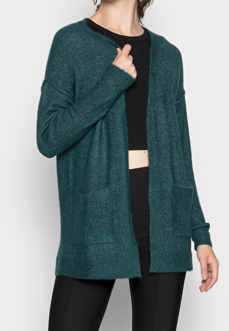 Cardigan turchese realizzato in materiale morbido, caratterizzato da una vestibilità comoda, apertura frontale, polsini a coste e due tasche frontali.
