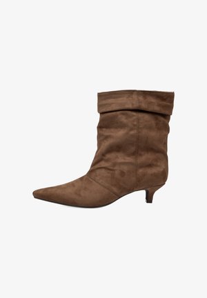 Bota marrón de ante hasta media pantorrilla con punta puntiaguda, caña holgada y tacón corto de tipo kitten, mostrada en perfil lateral derecho sobre fondo blanco.