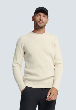Cream ribbed knit sweater with a round neck and long sleeves, paired with black pants. The fabric appears soft with a textured finish.
