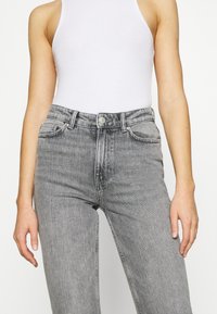 Jeans de mezclilla gris con cintura alta, diseño de cinco bolsillos y un ligero desgaste. Cuenta con un cierre de botón y corte recto.