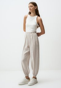 Lichte, geribbelde witte tanktop gecombineerd met losse, lichtbeige broek met elastische tailleband en boorden. Witte sneakers maken de look compleet.