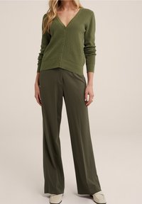 Khaki zelený pletený kardigan s výstřihem do V, s knoflíkovými zapínáními a žebrovanými manžetami, spárovaný s volnými kalhotami a krémovými mokasíny.