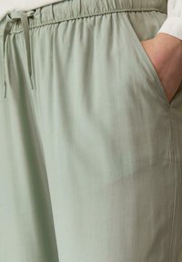 Pantalons légers de couleur vert clair, dotés d'une taille élastique avec cordon de serrage, avec des poches latérales et une texture lisse et mate.