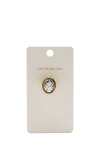 Pierścionek w kolorze złotym z teksturowanym, srebrnym środkiem, wyeksponowany na beżowej karcie z napisem "EDYCJA LIMITOWANA". Okrągły wzór, skomplikowane detale.