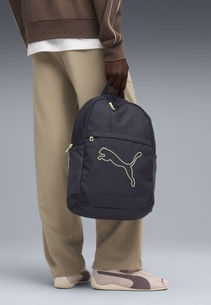Navy backpack made of durable fabric, featuring a prominent yellow Puma logo, front zip pocket, and mesh side pockets.