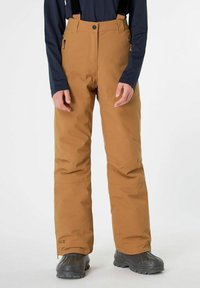 Pantaloni da neve marroni con bretelle nere regolabili, tasche con zip e design con gamba dritta. Indossati sopra stivali neri. Tessuto impermeabile.