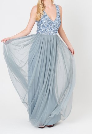 Kobieta w bezrękawniku z srebrnymi cekinami i zwiewną, jasno-niebieską tiulową spódnicą, trzymająca spódnicę na boki.