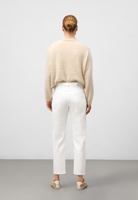 Beżowy puszysty sweter, białe proste dżinsy z tylnymi kieszeniami, zestawione z neutralnymi sneakersami, widziane z tyłu na jasnym tle.