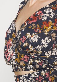 Top crop floral em azul marinho, com decote em V, mangas curtas, bainha franzida e padrão de flores multicoloridas, em tecido texturizado.