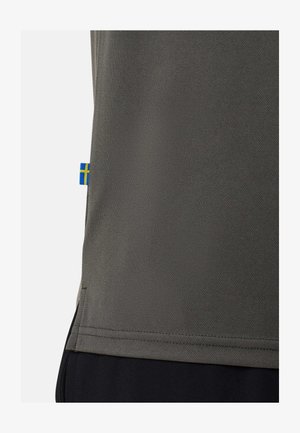 Szary teksturowany materiał spód części koszuli z małą szwedzką flagą na boku, noszony na czarnych spodniach.