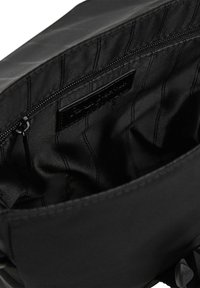 Interno in nylon nero di una borsa, dotato di una tasca con zip e una trama liscia con cuciture verticali e un'etichetta di marca.