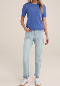 Blå strukturerad stickad kortärmad topp som är kombinerad med ljusblå raka jeans och vita sneakers med grå och tan accenter.