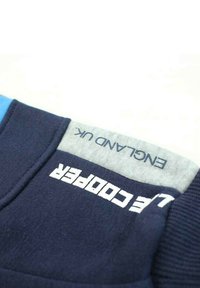 Sweatshirt marine avec des accents bleu clair et gris. Présente un tissu texturé, des blocs de couleur horizontaux et un texte imprimé blanc portant le mot "COOPER."