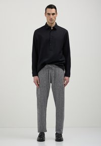 Chemise noire à manches longues avec plastron boutonné, assortie à un pantalon gris texturé avec poches et taille à cordon de serrage. Chaussures noires.