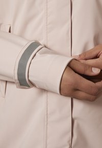 Svetle růžová rukávová část bundy s hladkým povrchem, zdobená šedým akcentem. Detailní záběr na látku a manžetu.