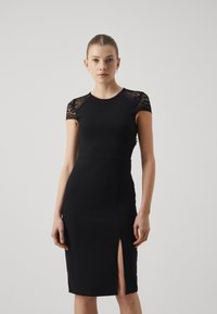 Svart klänning med korta spetsärmar, figursydd bodice och knälång fåll med en sidoöppning. Slät tyg med en elegant design.