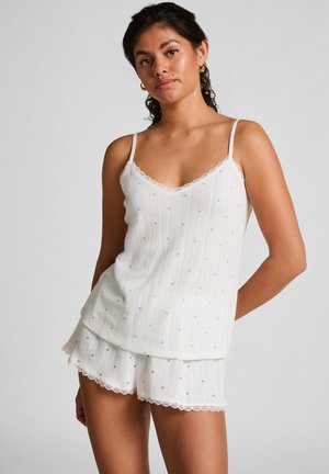White cotton sleep set featuring a spaghetti strap top with scalloped lace trim and blue heart prints, paired with matching shorts.