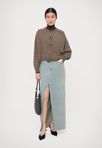 Brown knitted cardigan with button front, paired with a light blue denim maxi skirt featuring a side slit. Black handbag and heels included.