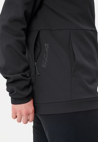 Giacca tecnica nera con superficie textrurata, dotata di tasca con zip e cordino regolabile sull'orlo per una vestibilità aderente.