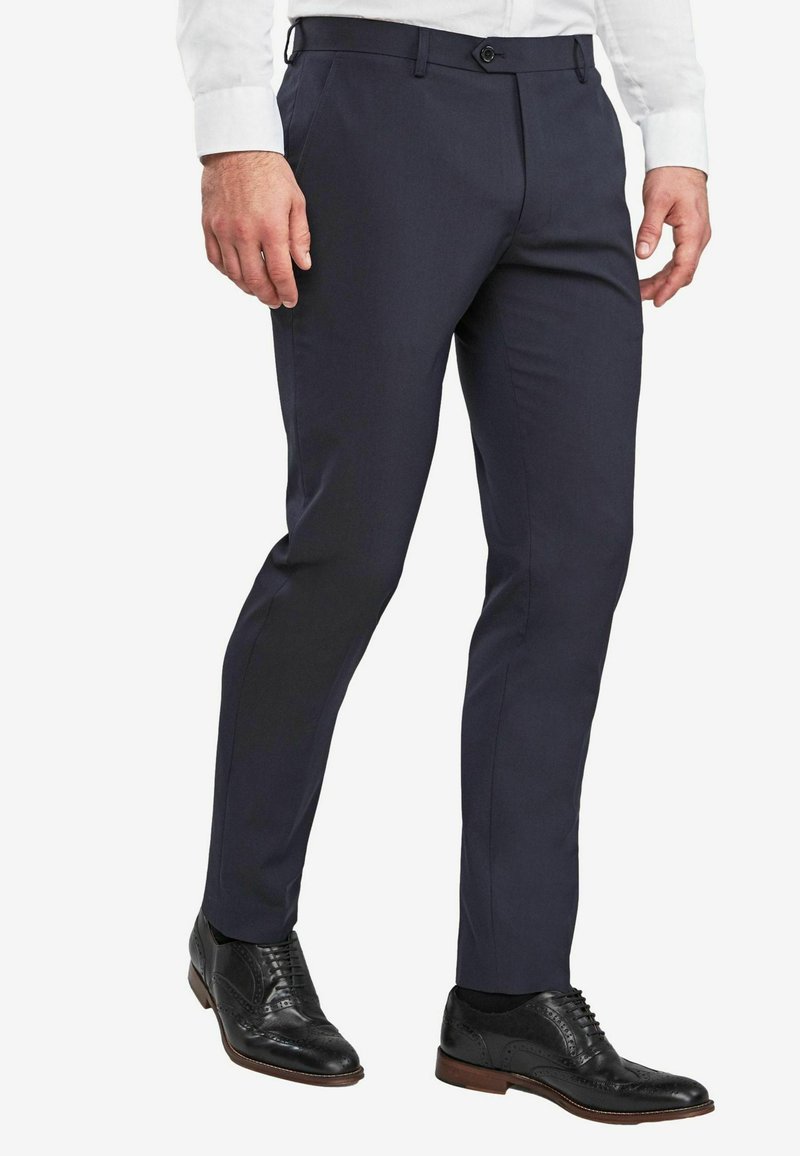 Tengerészkék elegáns nadrág karcsúsított fazonban. Sima anyagból készült, oldalán zsebekkel és övbújtatóval, fekete brogue cipővel párosítva.