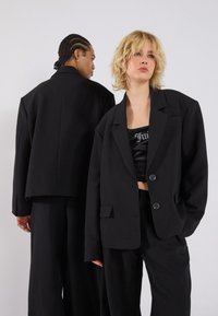 Zwarte outerwear met een oversized ontwerp, twee knopen en een gestructureerde kraag. Gestyled met een wijdvallende broek. Gladde textuur.