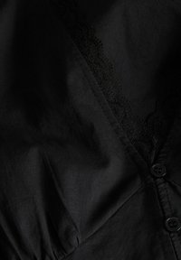 Gros plan sur un tissu noir avec un bord en dentelle le long d'un décolleté en V et deux boutons noirs sur le côté droit.