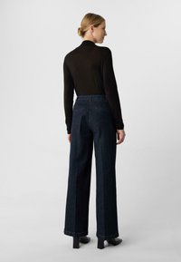 Granatowe dżinsy o szerokich nogawkach z wysokim stanem, wykonane z teksturowanego denimu, z prostymi szwami, zestawione z dopasowanym czarnym topem z długim rękawem.