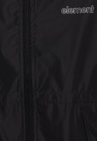 Black jacket featuring a front zipper and side pockets, made from smooth fabric with a subtle sheen and an embroidered logo in white.