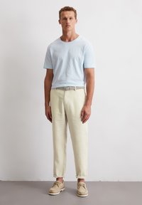 Helles blaues Baumwoll-T-Shirt, lockere Passform, kombiniert mit off-white Leinenhosen. Abgerundet mit beigen Schuhen und einem gewebten Gürtel.