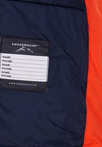 Marinblå och orange jacka i tyg med en svart etikett som har en bergslogotyp och plats för namn och telefonnummer. Mjuk och hållbar textur.