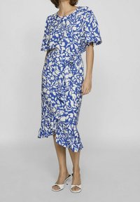Šaty s květinovým potiskem v modré a bílé barvě, s krátkými rukávy, zavazováním v pase a volánkovým lemem. Lehká látka s plynulou siluetou.