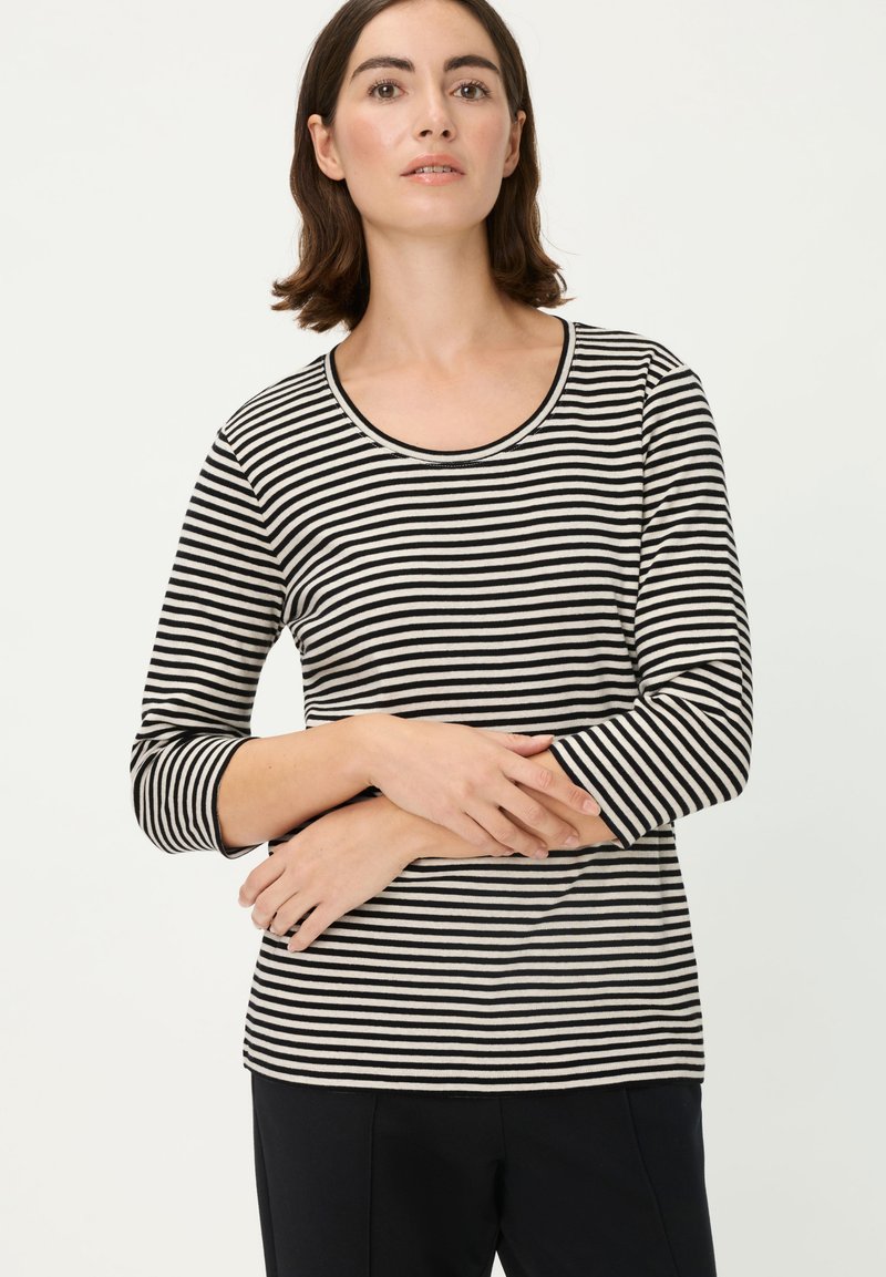 Schwarz-weiß gestreiftes Langarmshirt mit rundem Ausschnitt und tailliertem Schnitt, präsentiert über dunkler Hose. Weiche Stoffstruktur, legeres Design.