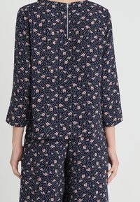 Blusa floreale con sfondo navy e fiori rosa, maniche a 3/4 e chiusura con zip sul retro per un facile indossamento.