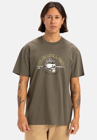 Camiseta de algodón verde oliva con un diseño gráfico de calavera rodeada de plantas, cuello redondo, mangas cortas y corte holgado.