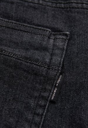 Schwarzer Denimstoff mit einer Gesäßtasche, sichtbaren Nähten und einem kleinen schwarzen Stoffetikett mit dem Schriftzug "ombre denim".