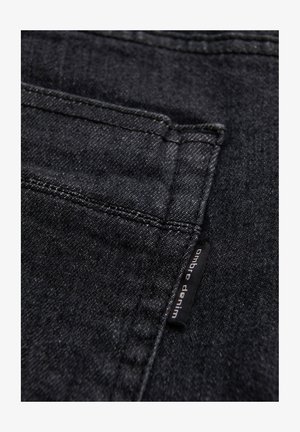 Sort denimstof med en baglomme med synlige sømme og et lille sort stofmærke med teksten "ombre denim".