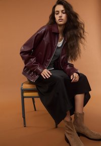 Giacca in pelle bordeaux con chiusura a zip, gonna nera in satin e stivaletti beige in suede. Tessuto liscio e design a vestibilità rilassata.